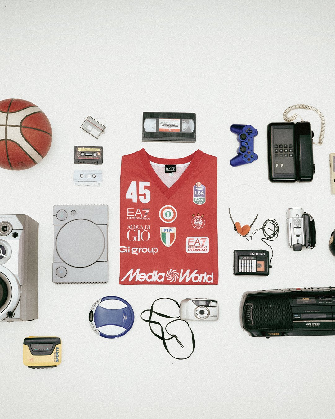 La maglia ufficiale di Olimpia Milano circondata da oggetti tecnologici iconici degli anni 90